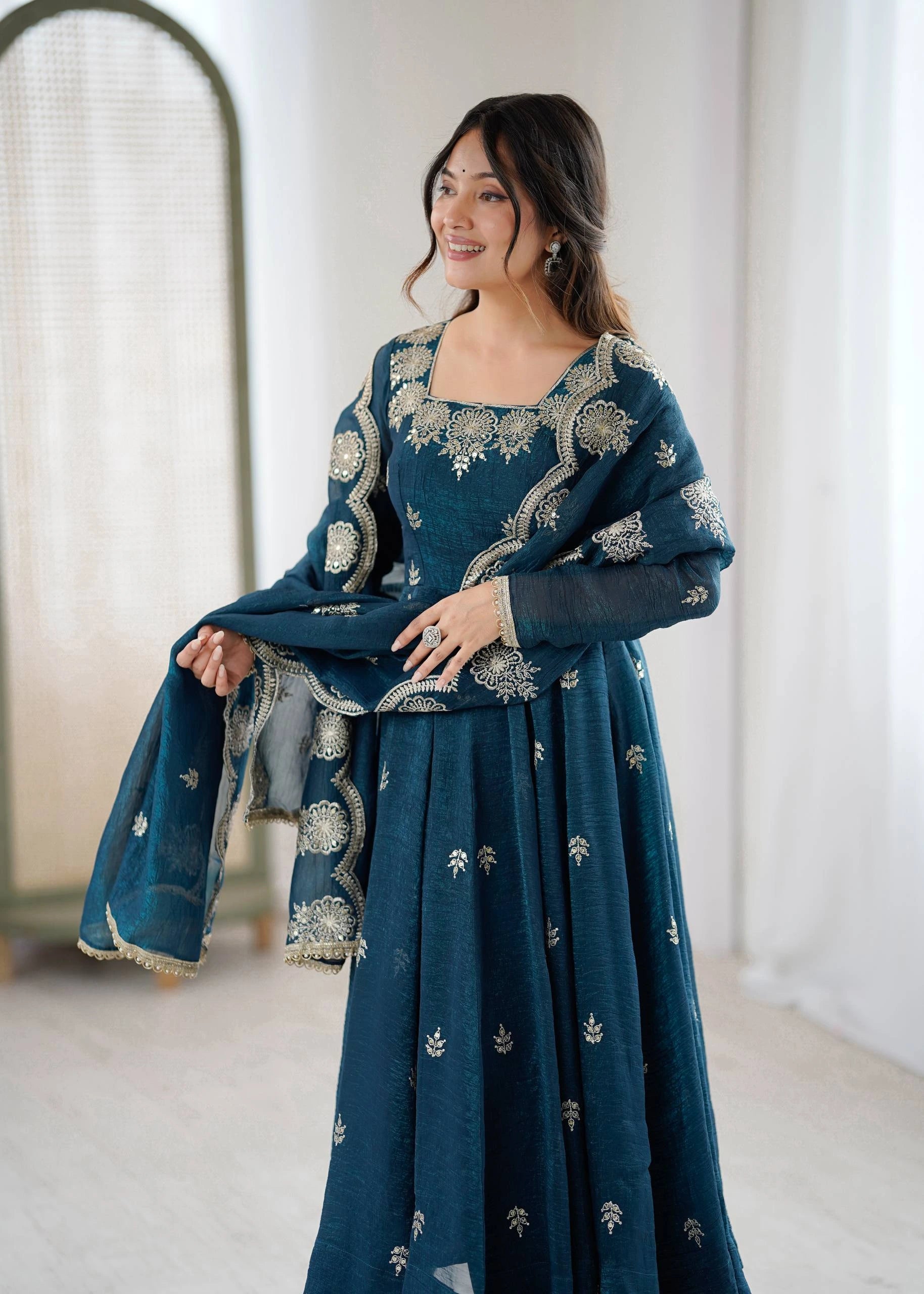 Woman wearing a teal embroidered dress in a minimal indoor setting