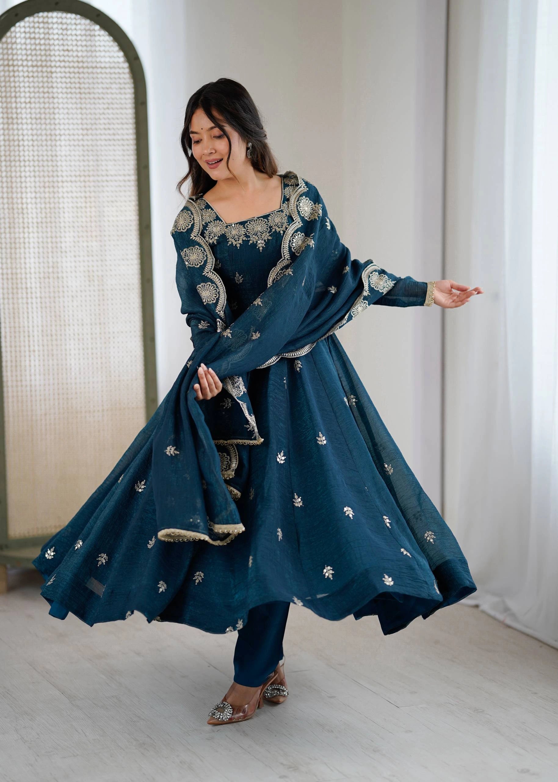 Woman in a blue embroidered traditional outfit standing indoors.
