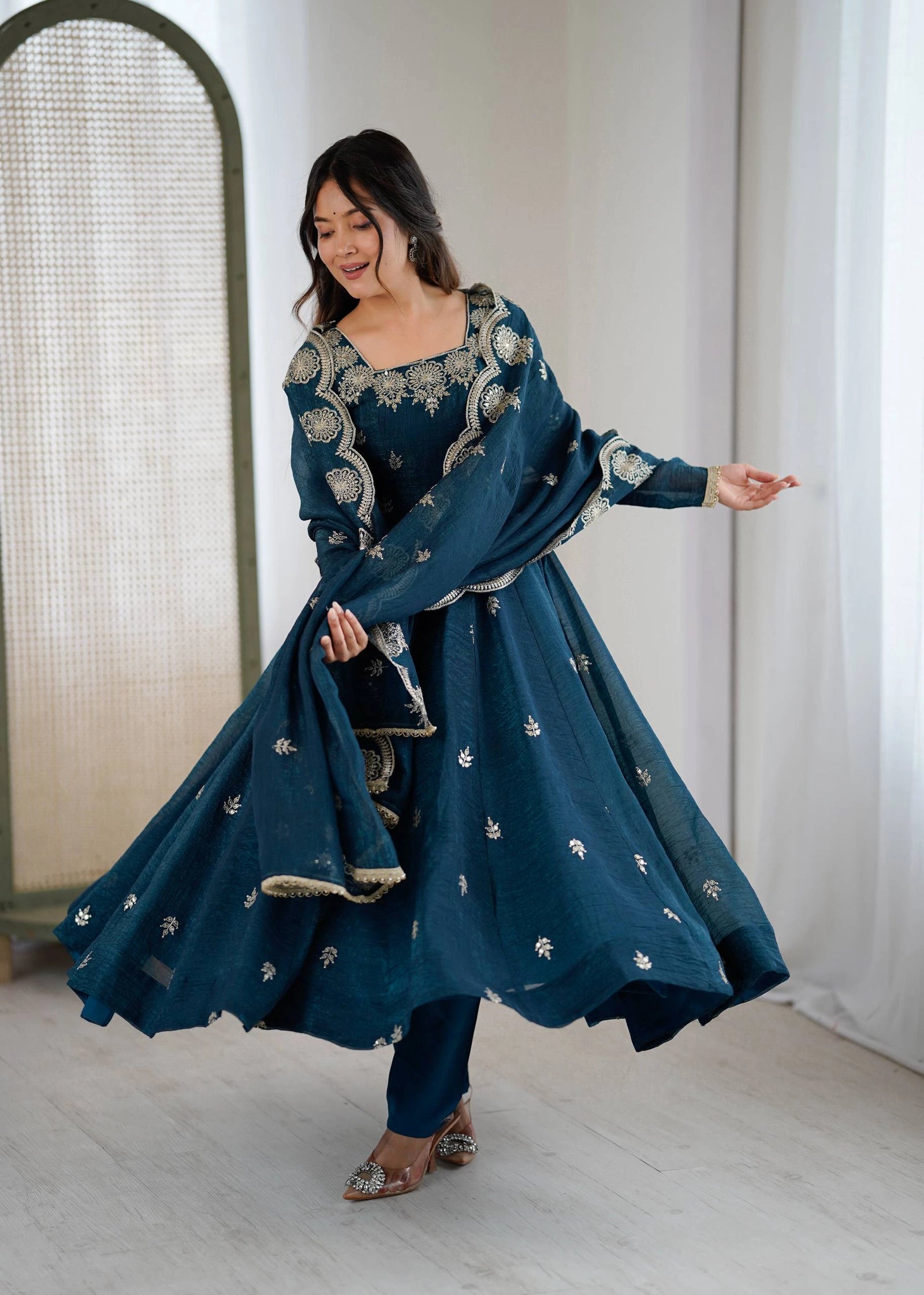 Woman in a blue embroidered traditional outfit standing indoors.