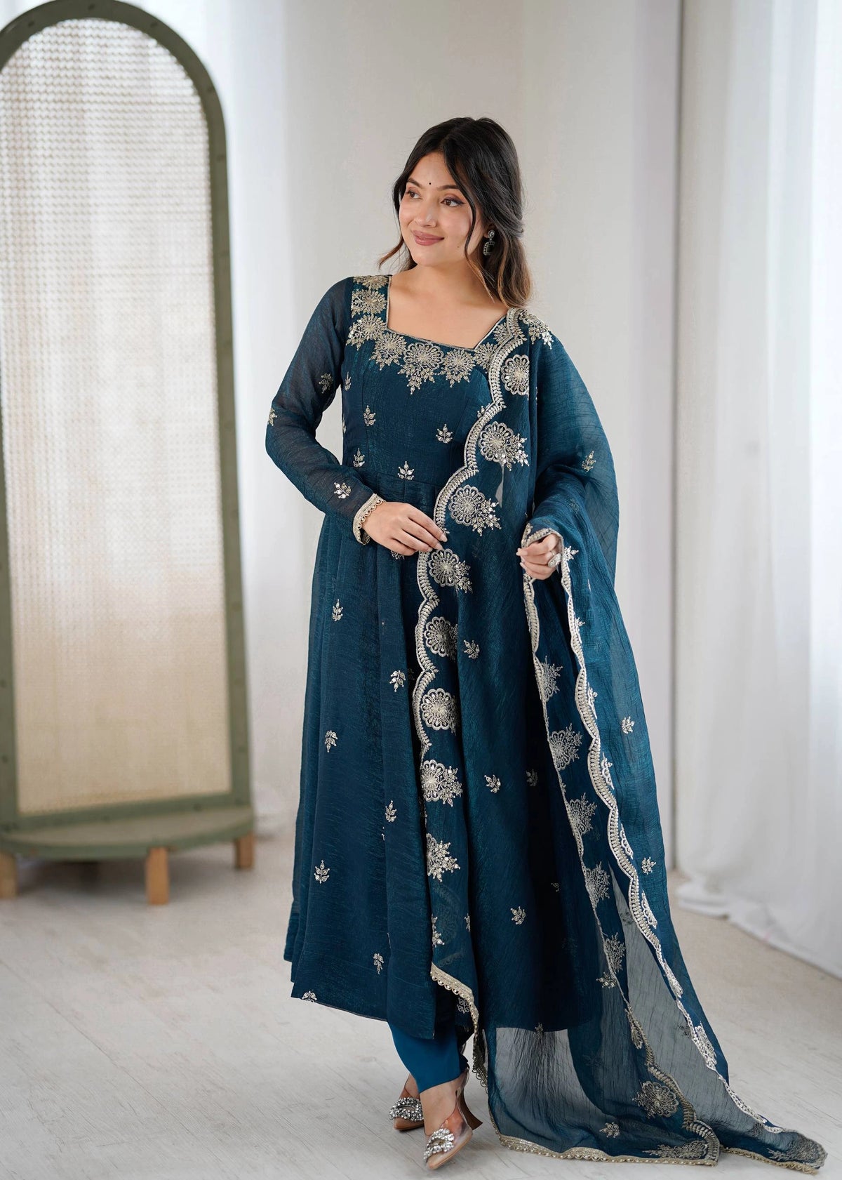 Woman wearing a teal embroidered traditional outfit with a white background