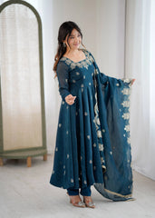 Woman wearing a teal embroidered outfit with a matching dupatta in a minimal indoor setting.