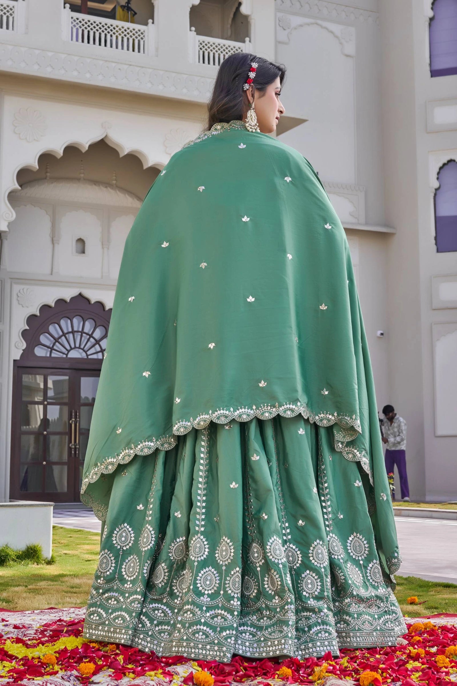 Woman in a green traditional outfit with white patterns standing in front of a building.