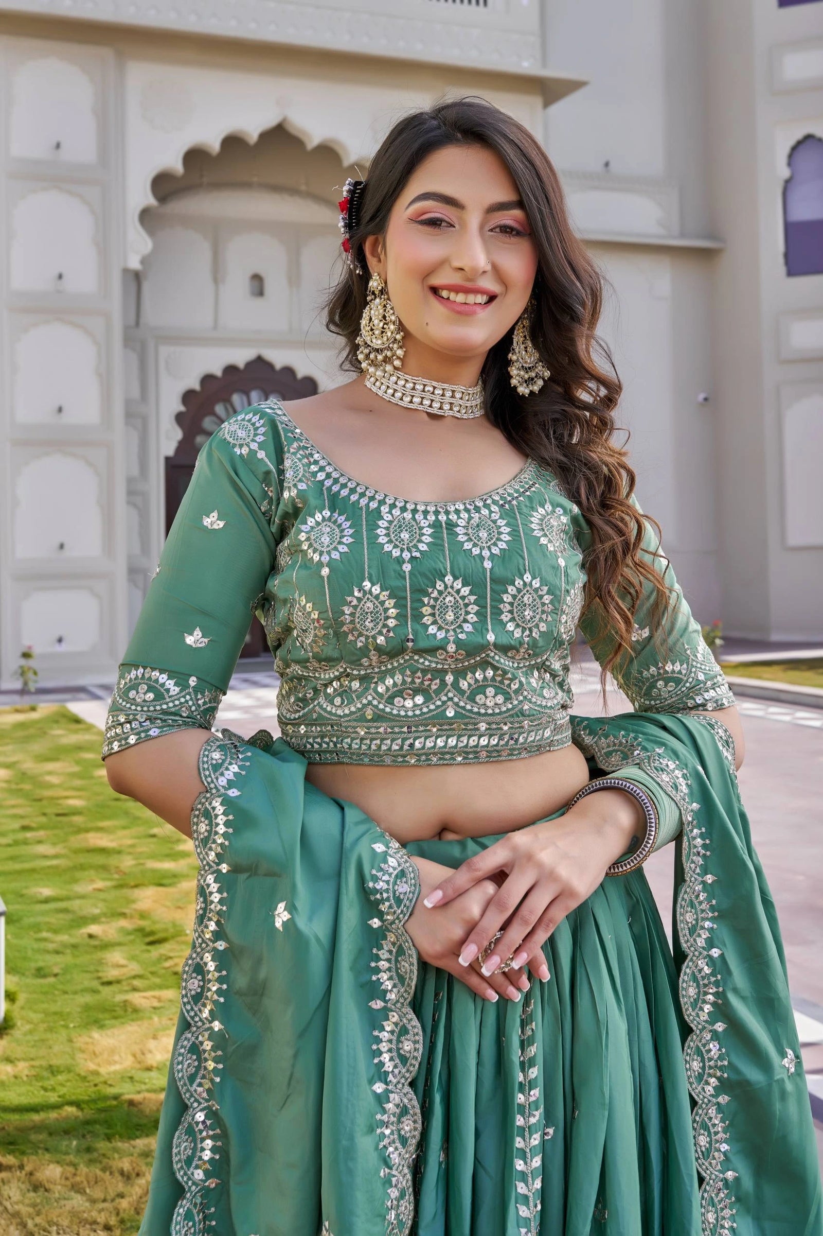 Woman in a green traditional outfit with intricate designs standing in front of an architectural structure.
