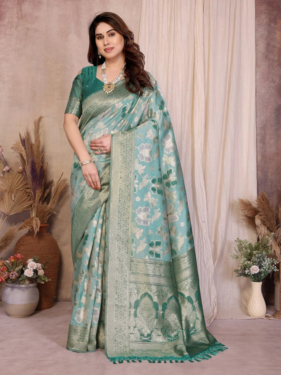 Woman wearing a green saree with a floral pattern in a decorated room.