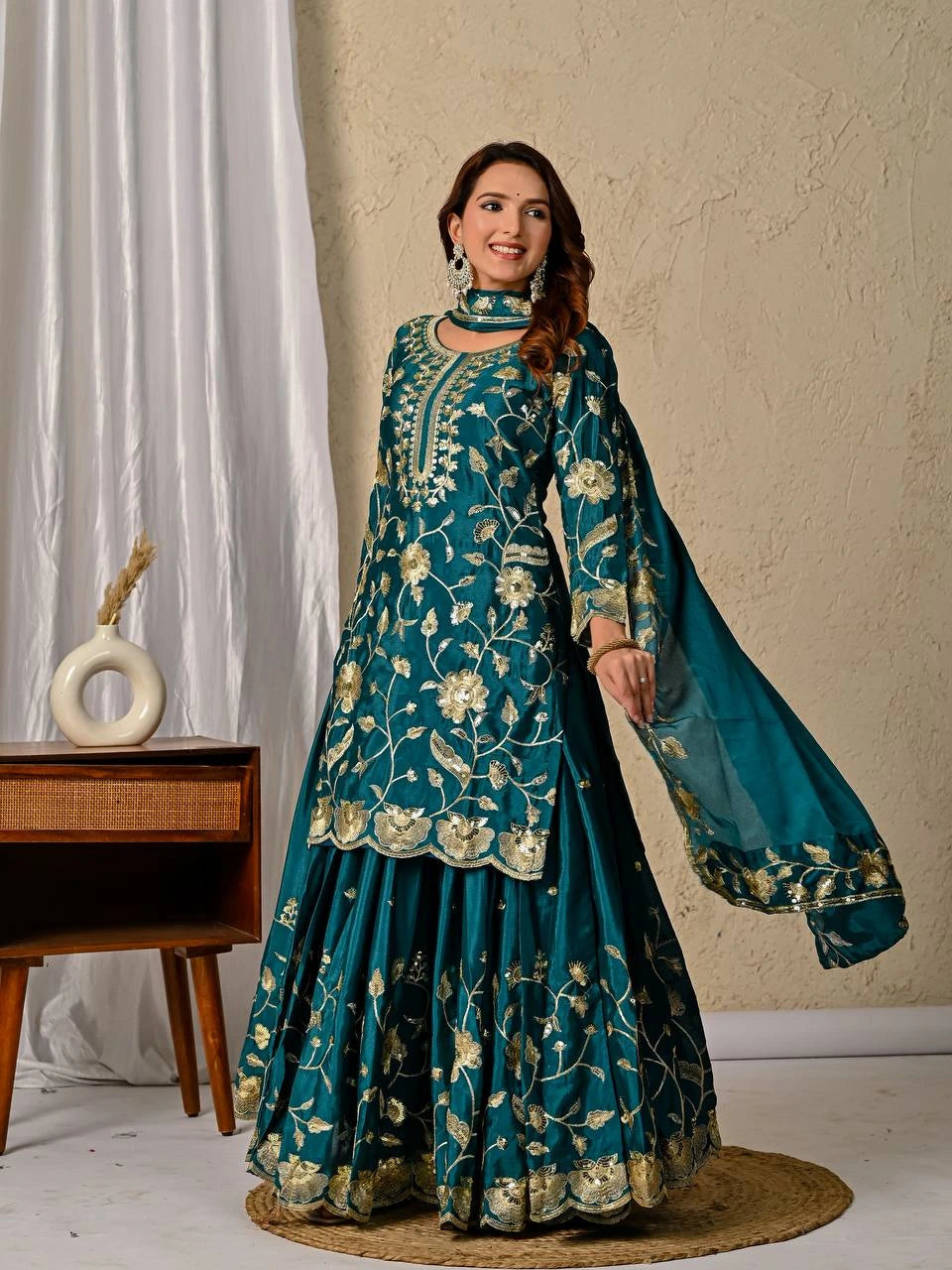 Woman wearing a teal embroidered traditional outfit with a beige background