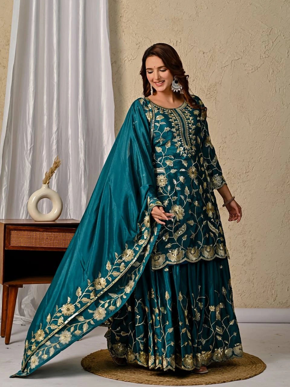 Woman wearing a teal embroidered traditional outfit with a matching dupatta in a neutral setting.