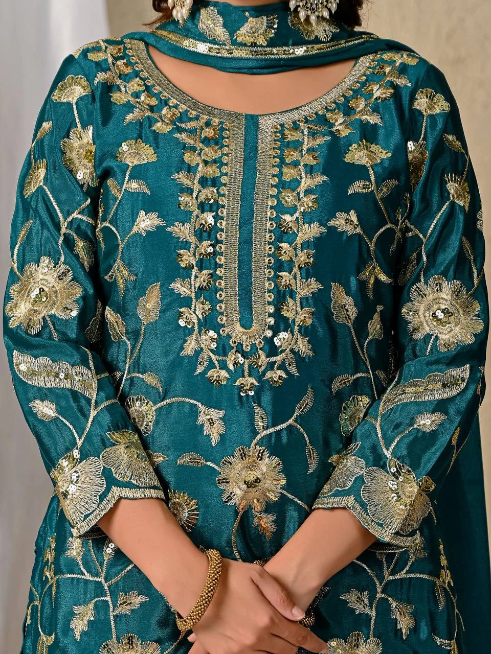 Teal embroidered garment with gold details on a plain background