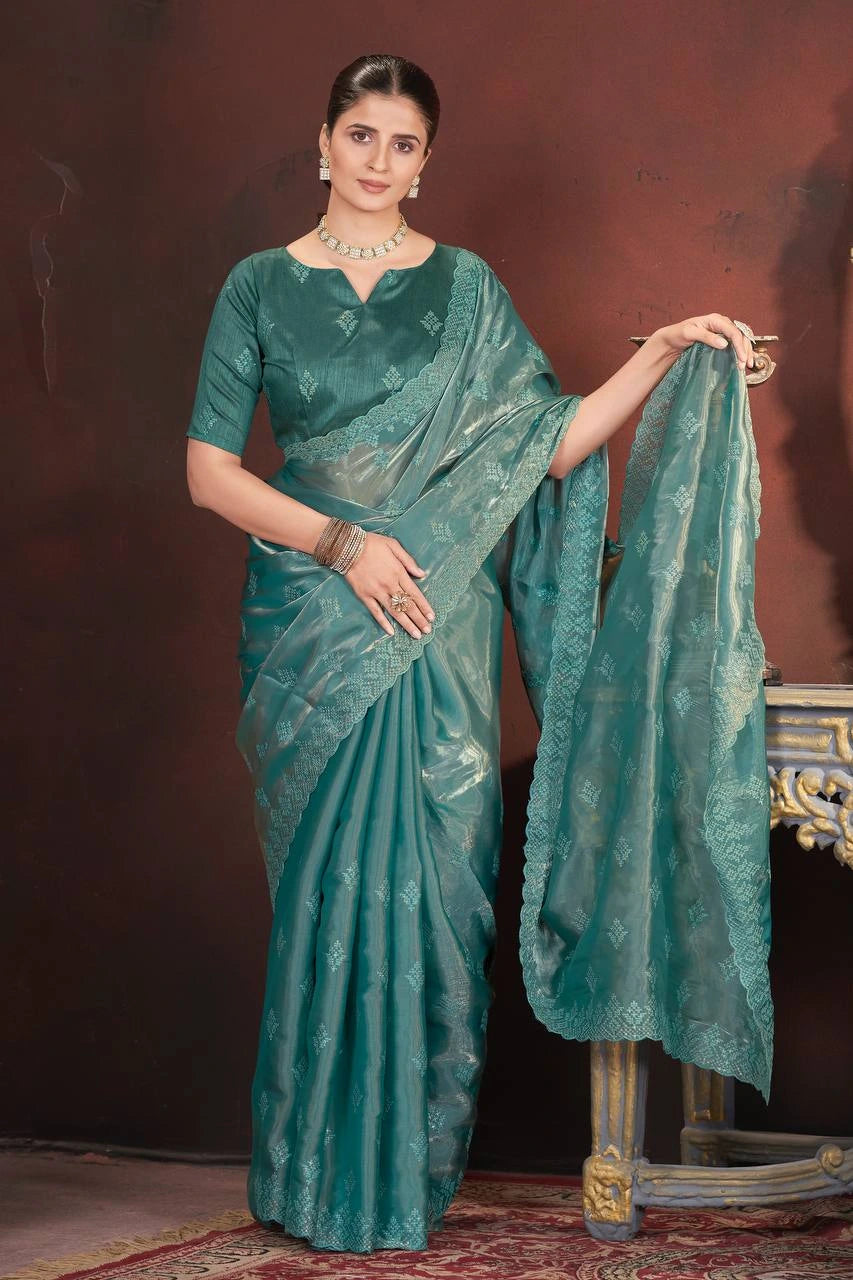 Woman in a teal saree holding it with a dark background