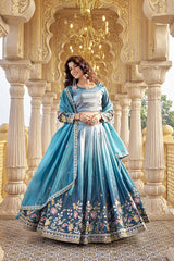 Woman in a blue embroidered traditional outfit standing in an ornate architectural setting.