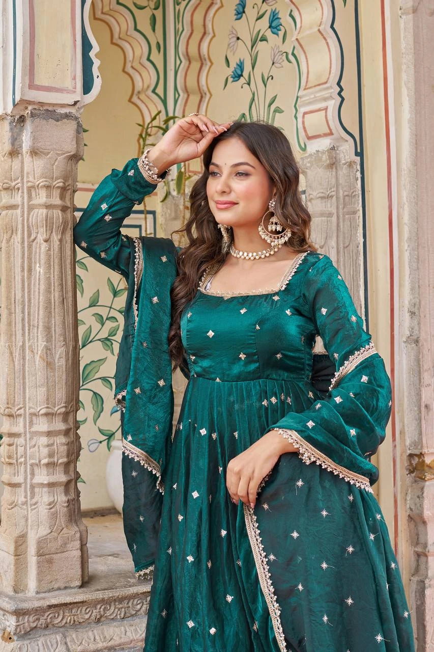 Woman in a green traditional outfit with intricate designs standing in front of decorative architecture.