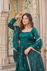 Woman in a green traditional outfit with intricate designs standing in front of decorative architecture.