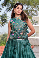 Woman in a green embroidered traditional outfit standing in front of a fountain.