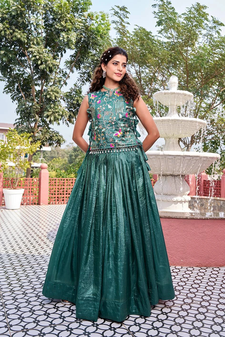 Woman in a green dress standing in front of a fountain with trees in the background