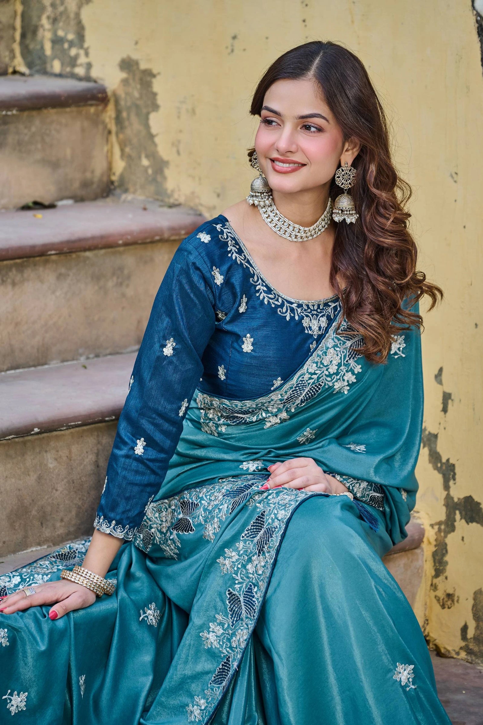 Woman in a blue saree with intricate patterns sitting on steps.