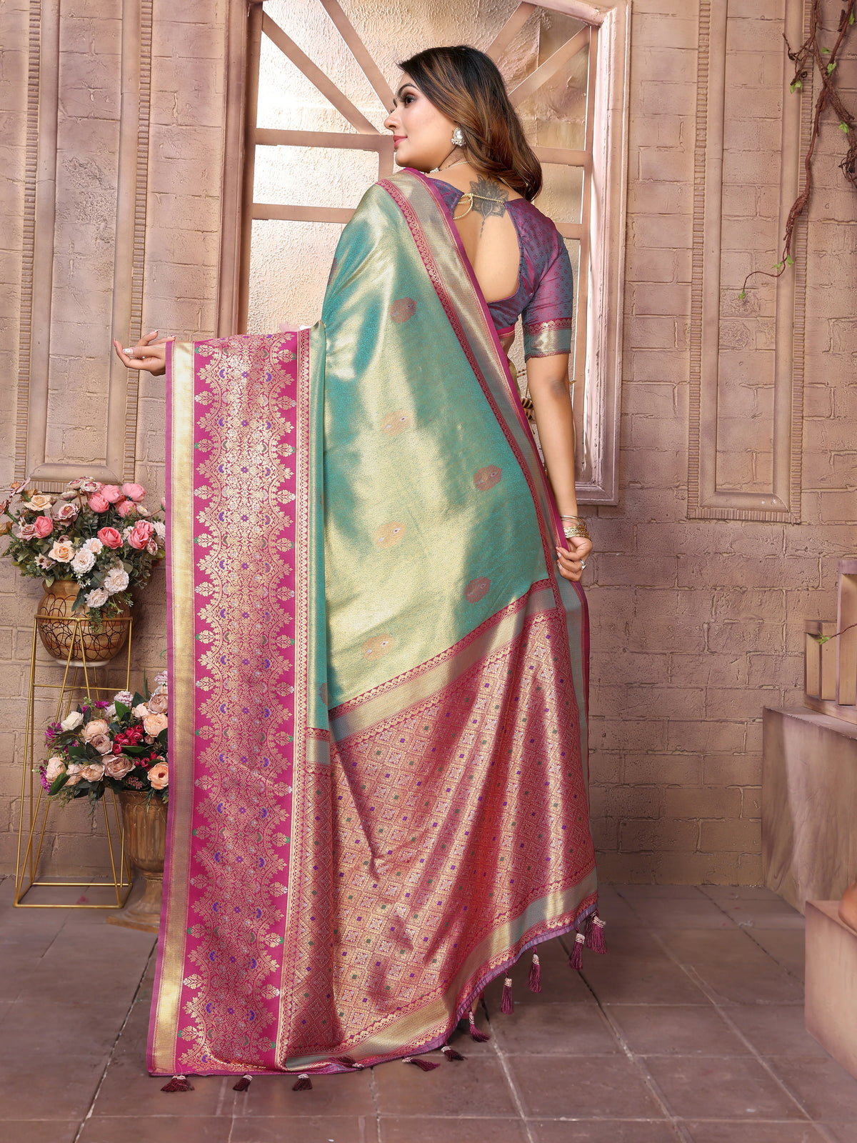 Woman wearing a traditional saree in a decorated indoor setting with flowers and decor.