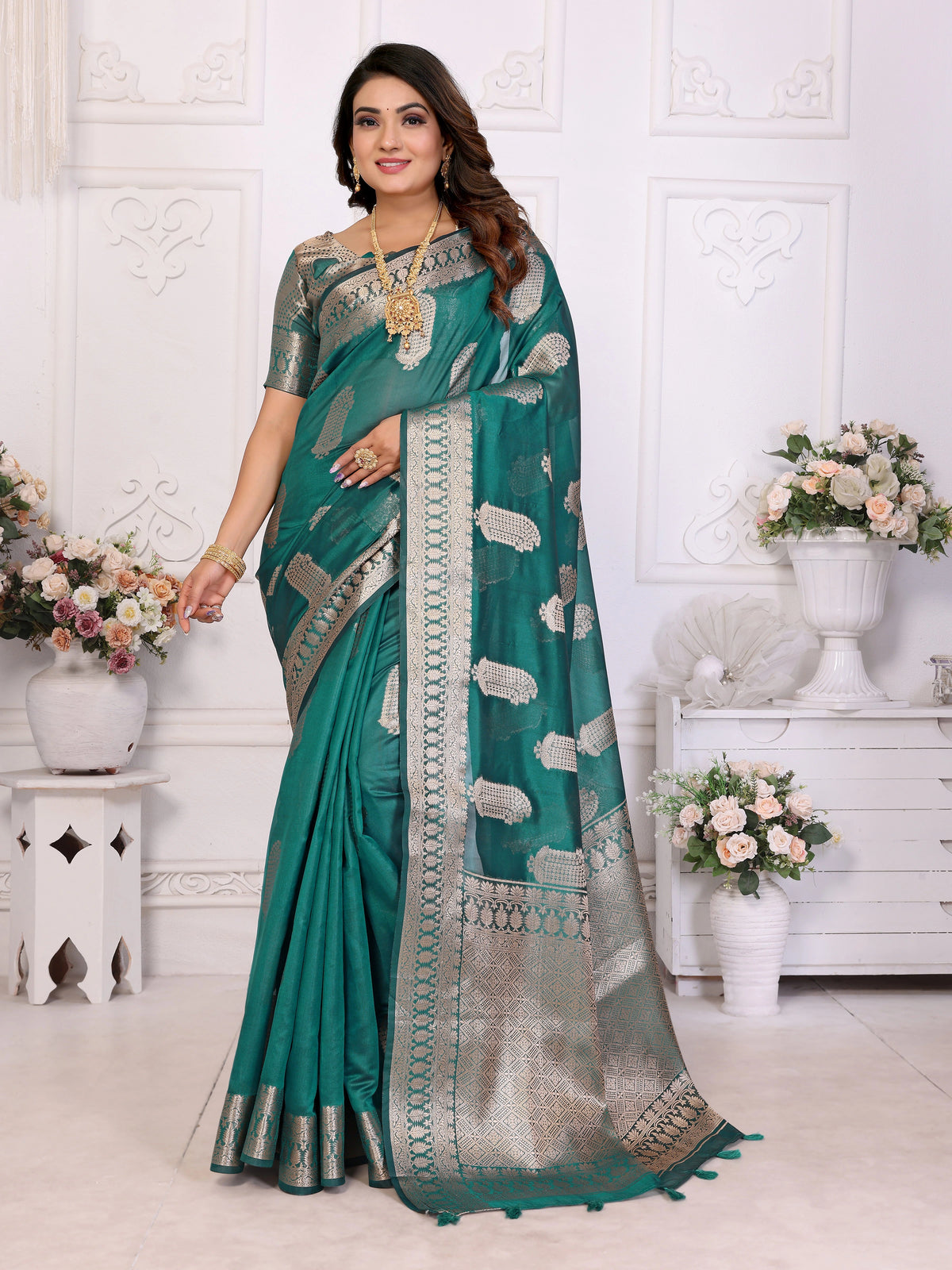 Woman wearing a teal saree with a white pattern in a decorated room.
