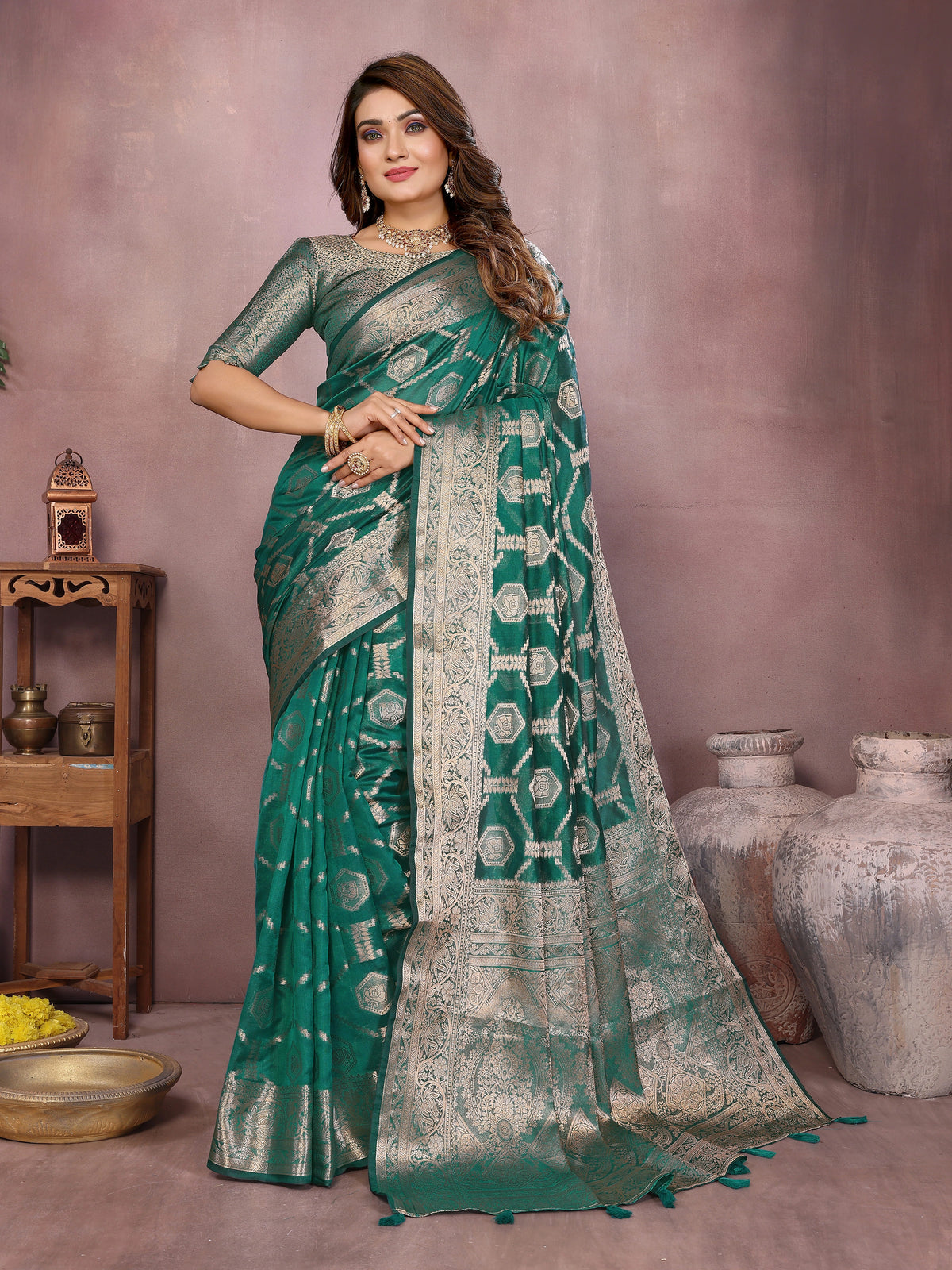 Woman wearing a green saree with a pattern, standing against a neutral background.