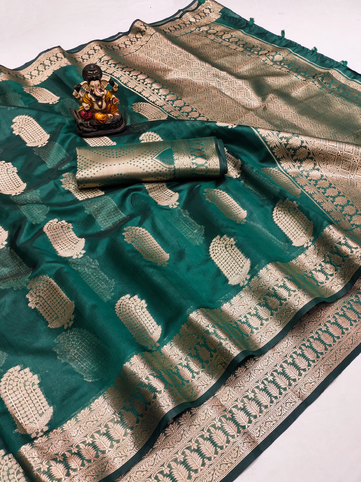 Teal saree with white patterns and a decorative item on a white background