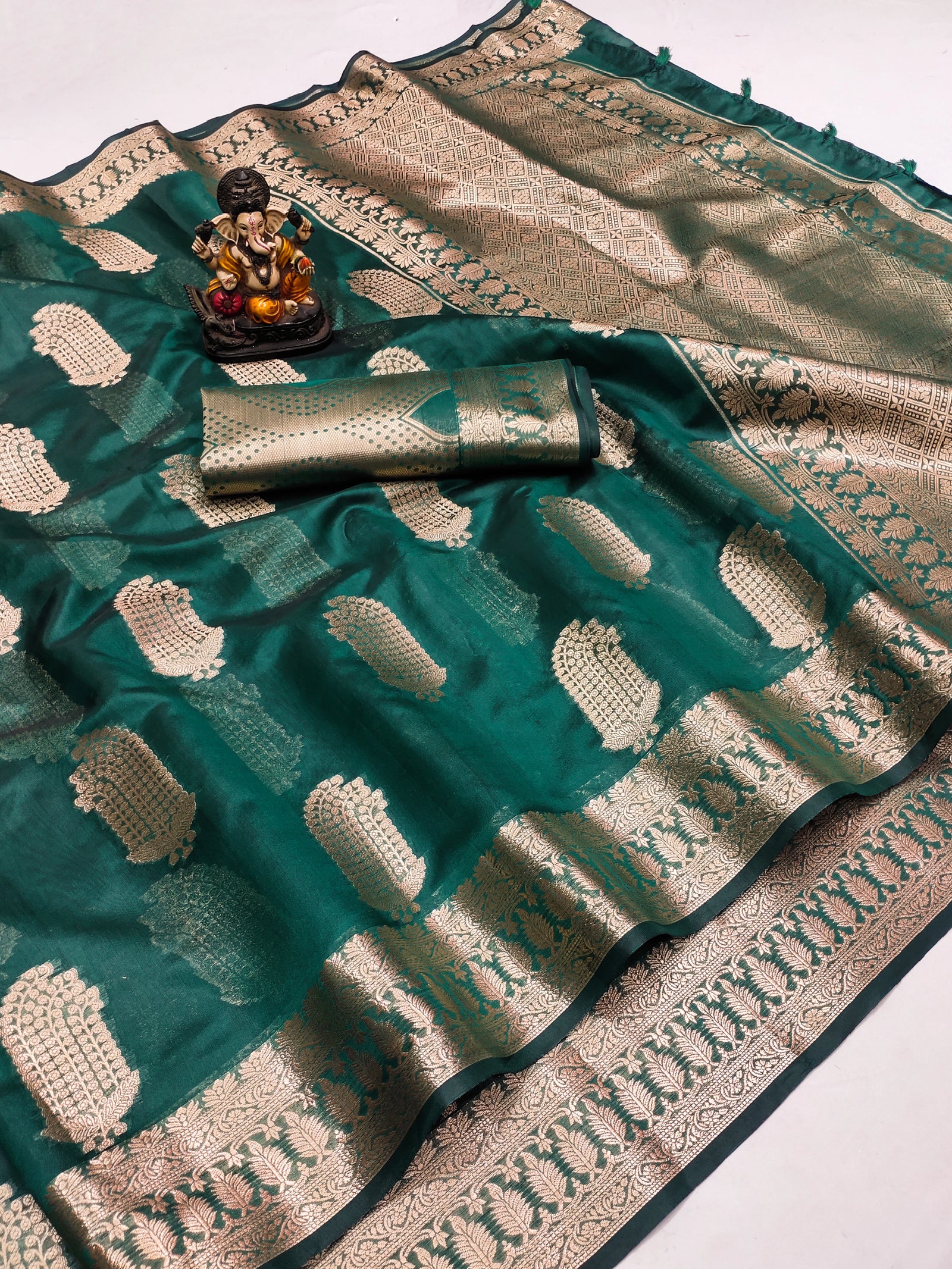 Teal saree with white patterns and a decorative item on a white background