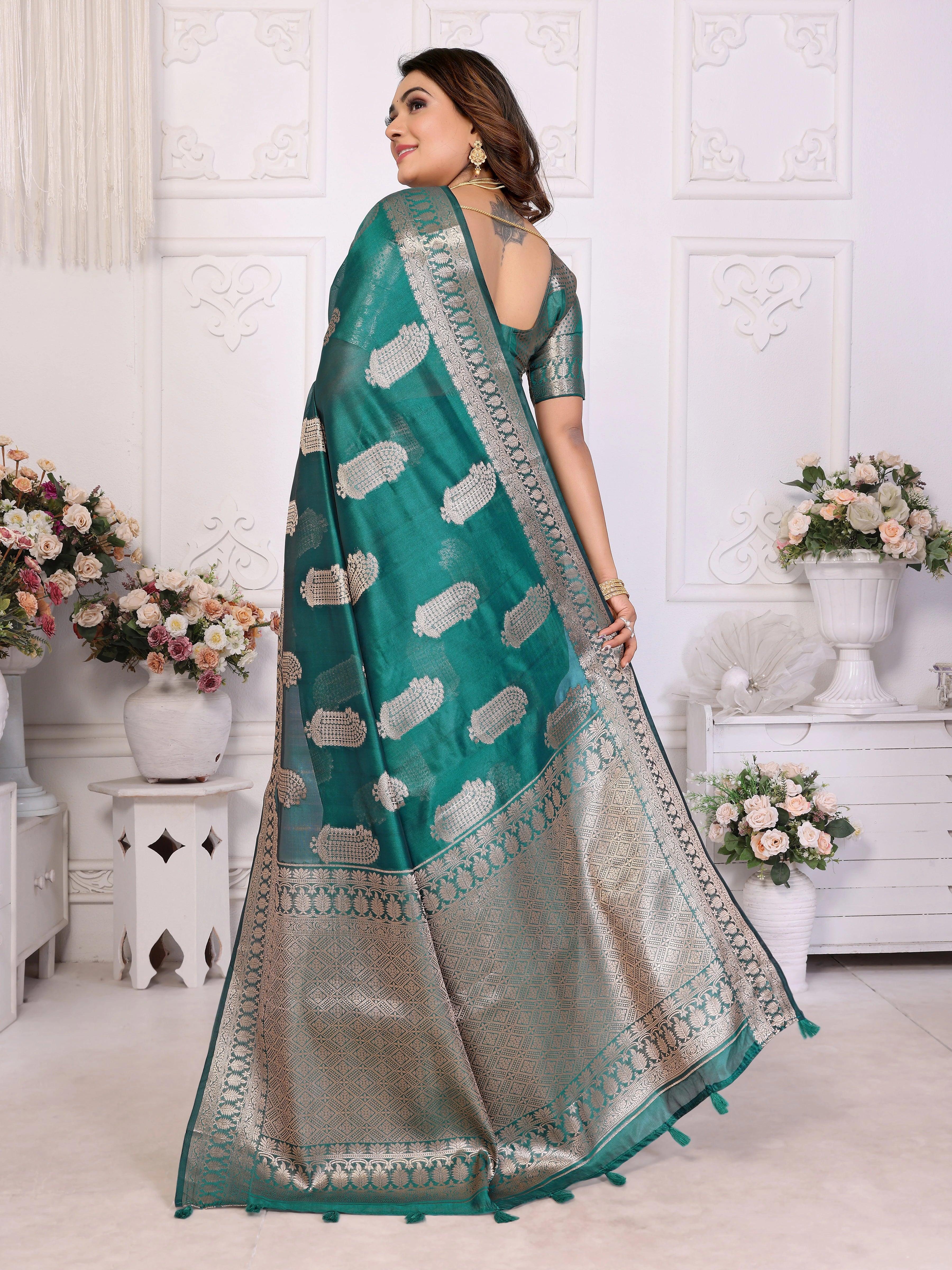 Woman wearing a teal saree with white patterns in a decorated room.