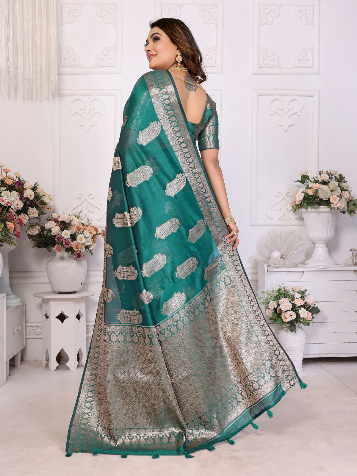 Woman wearing a teal saree with white patterns in a decorated room.