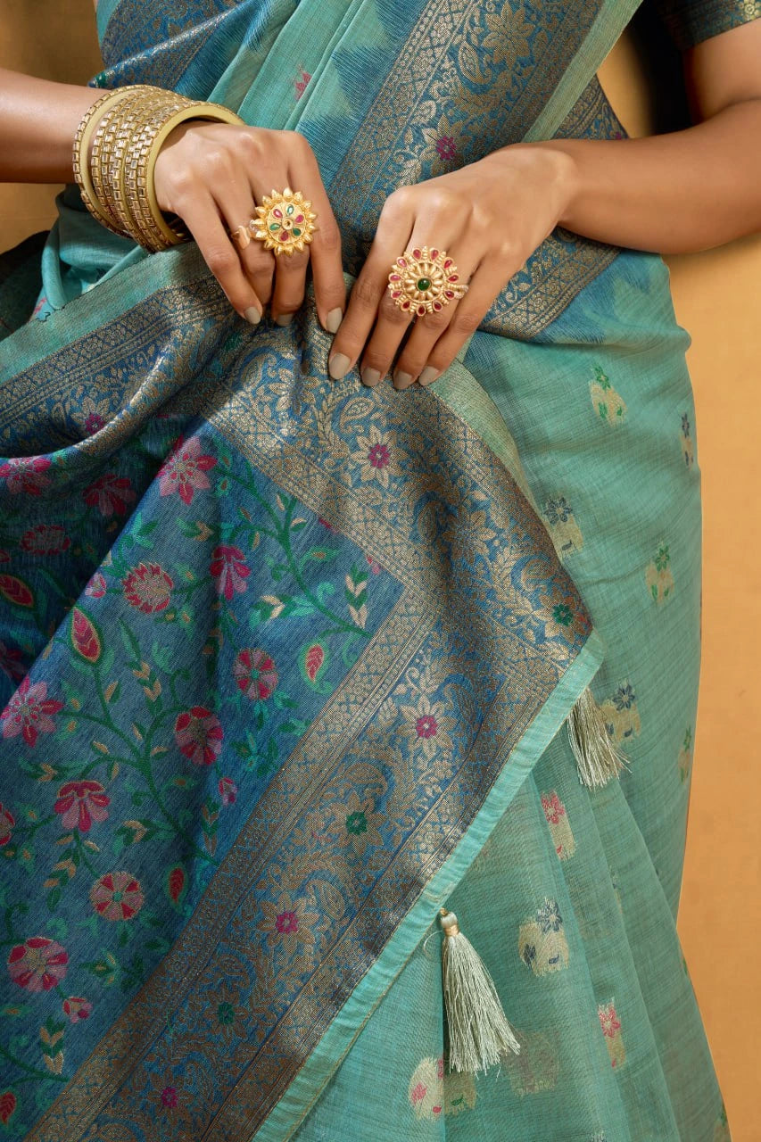 Close-up of a person wearing a teal saree with floral patterns, holding the fabric.