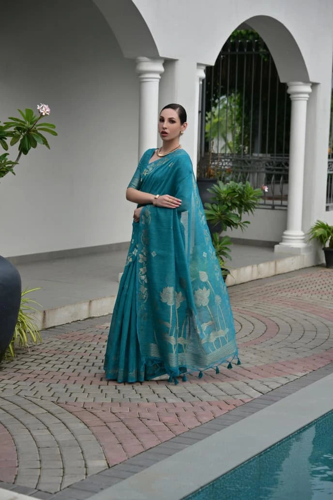 Woman in a teal saree standing in an outdoor setting with plants and a pool.
