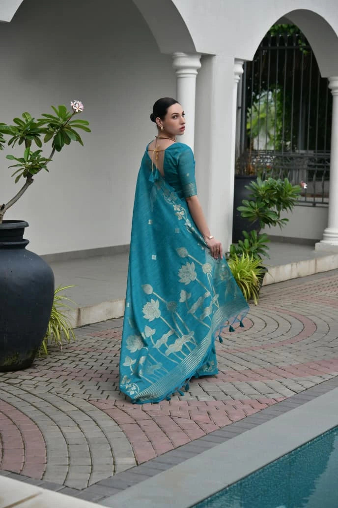 Woman in a blue saree standing by a poolside with plants around