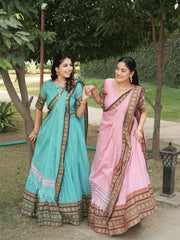 Two women in traditional sarees standing outdoors with trees and grass in the background.