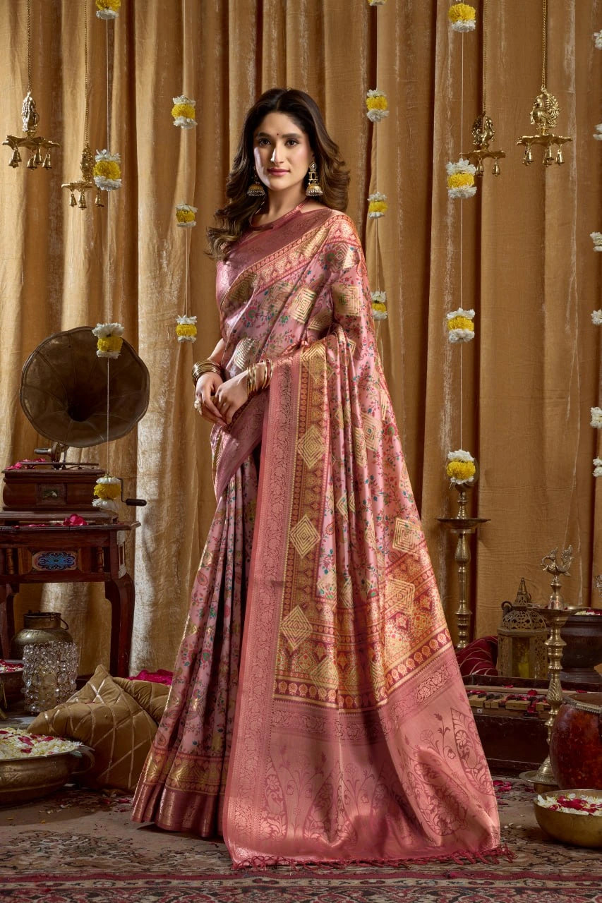 Woman in a pink saree with gold patterns standing in a decorated room.