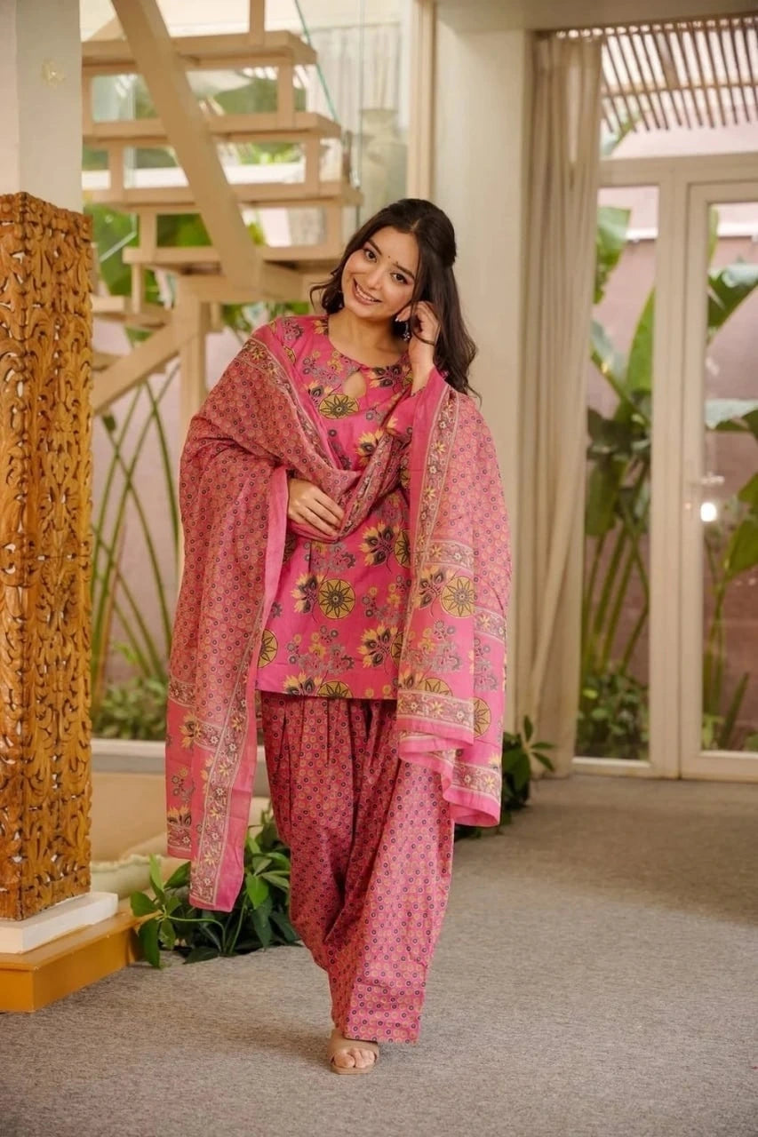 Woman in a pink traditional outfit standing indoors with decorative elements in the background