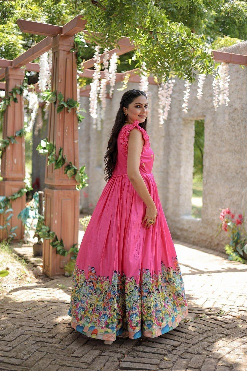 Woman in a pink dress with floral hem standing outdoors under a wooden archway.