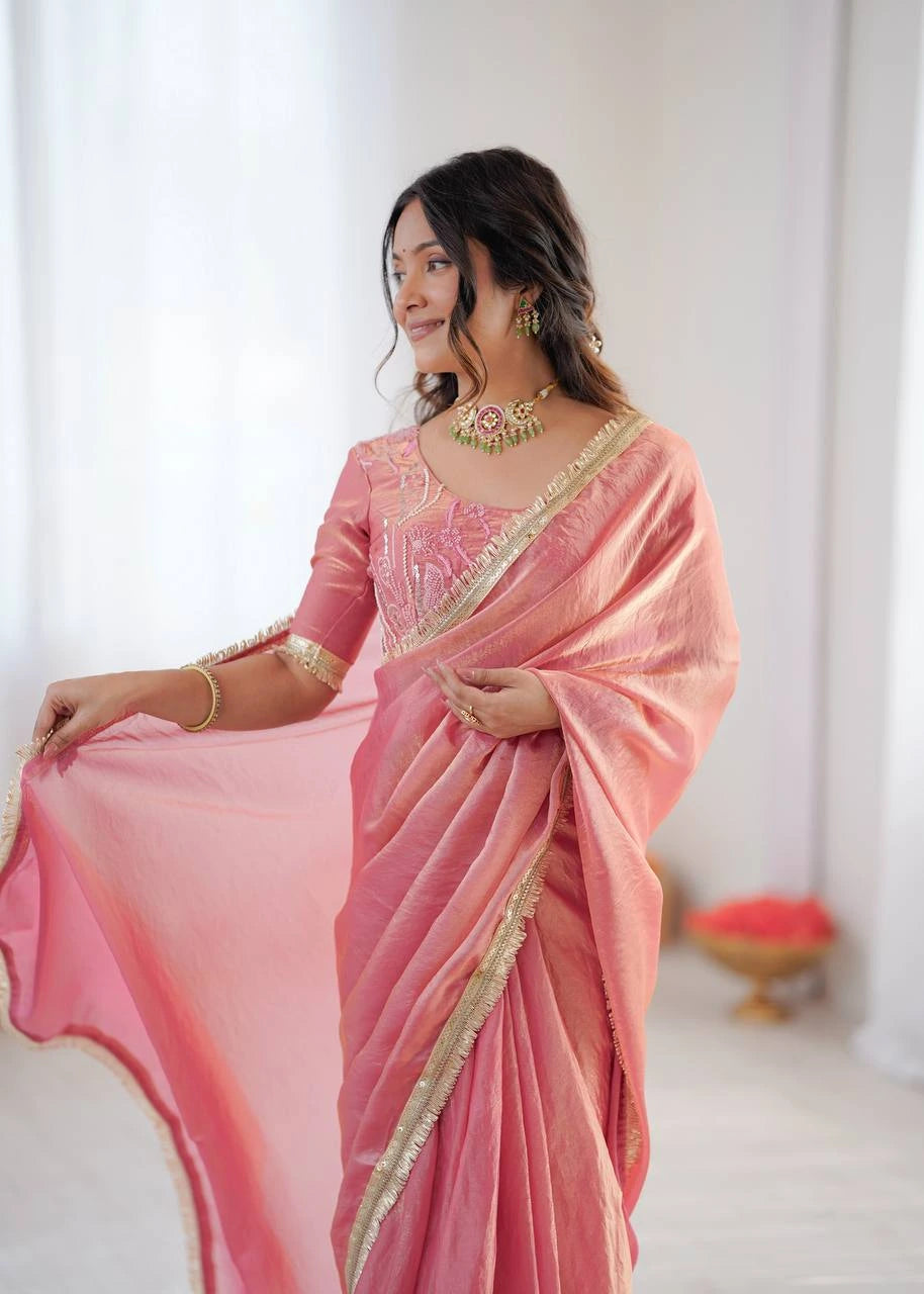 Woman wearing a pink saree with gold border against a white background