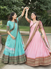 Two women in traditional sarees standing outdoors with greenery in the background