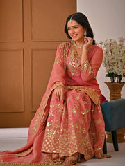 Woman in a pink and gold embroidered traditional outfit sitting on a chair.