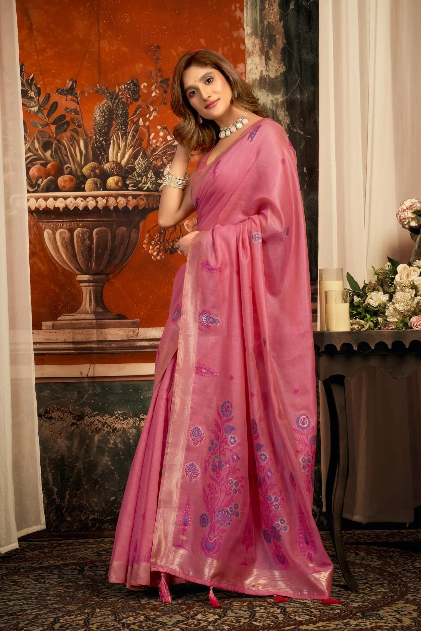 Woman in a pink saree standing in an elegant indoor setting with floral decorations.