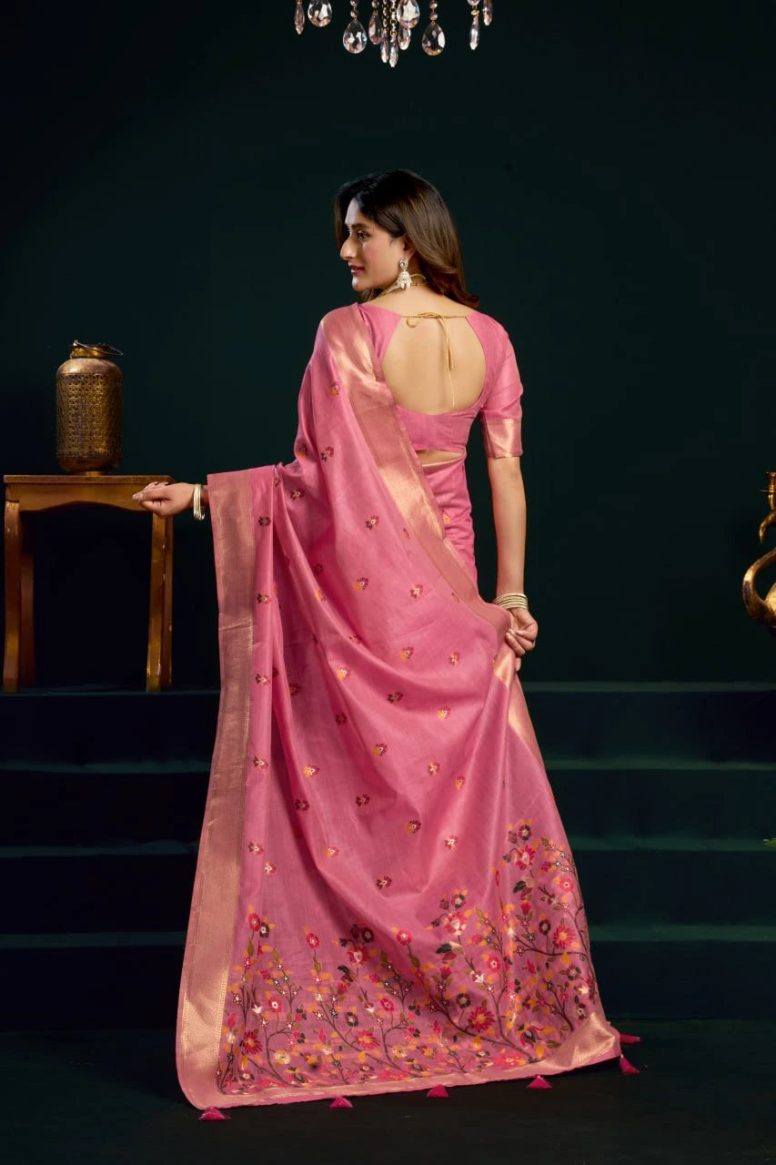 Woman in a pink saree with floral patterns standing in a dimly lit room.