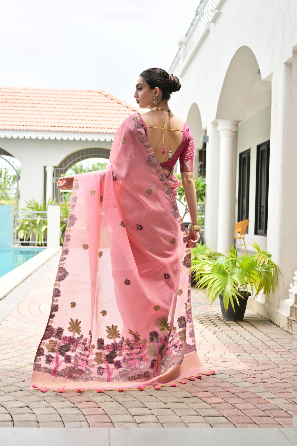 Woman in a pink saree standing by a poolside with a white building in the background