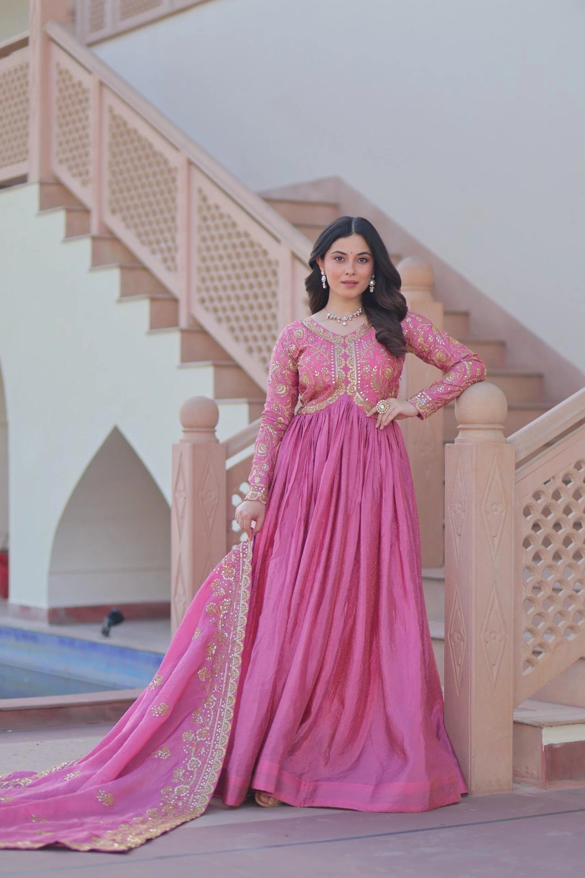 Woman in a pink traditional outfit standing in front of a staircase.