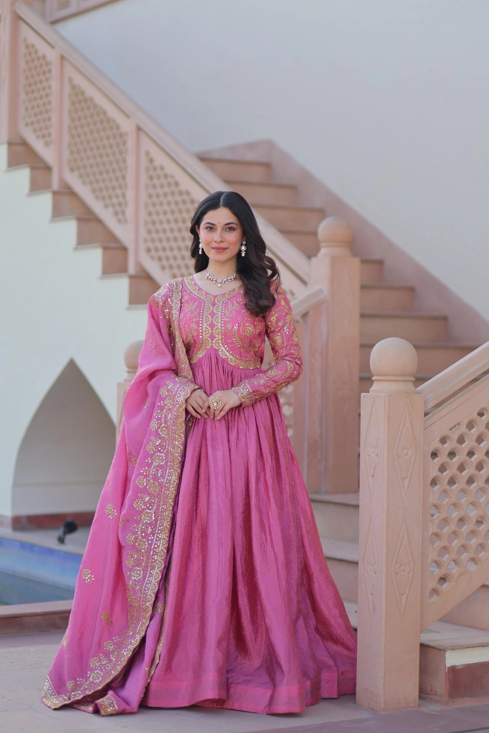 Woman in a pink traditional outfit standing in front of a staircase.