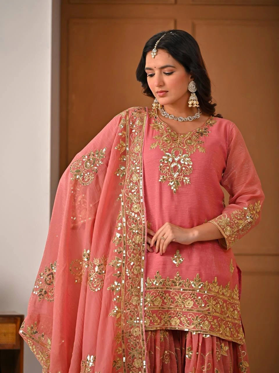 Woman wearing a pink traditional outfit with gold embroidery in a neutral setting