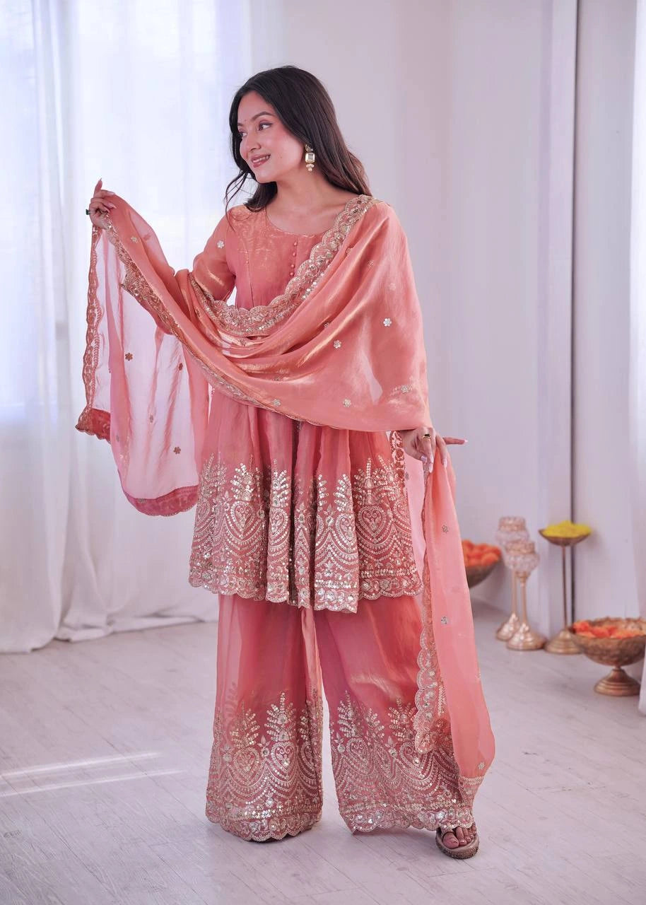 Woman in a traditional pink embroidered outfit with a matching dupatta, standing indoors.