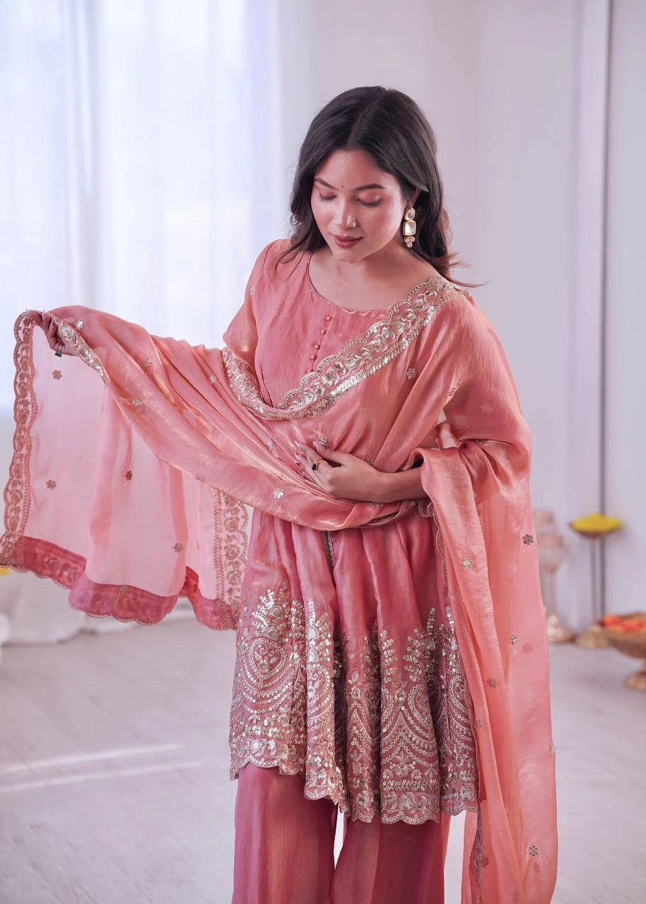 Woman wearing a traditional pink outfit with intricate embroidery in a bright room.