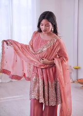 Woman wearing a traditional pink outfit with intricate embroidery in a bright room.