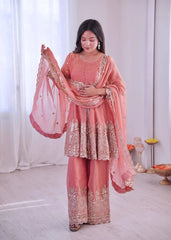 Woman in a traditional pink and gold outfit with a matching dupatta, standing indoors.