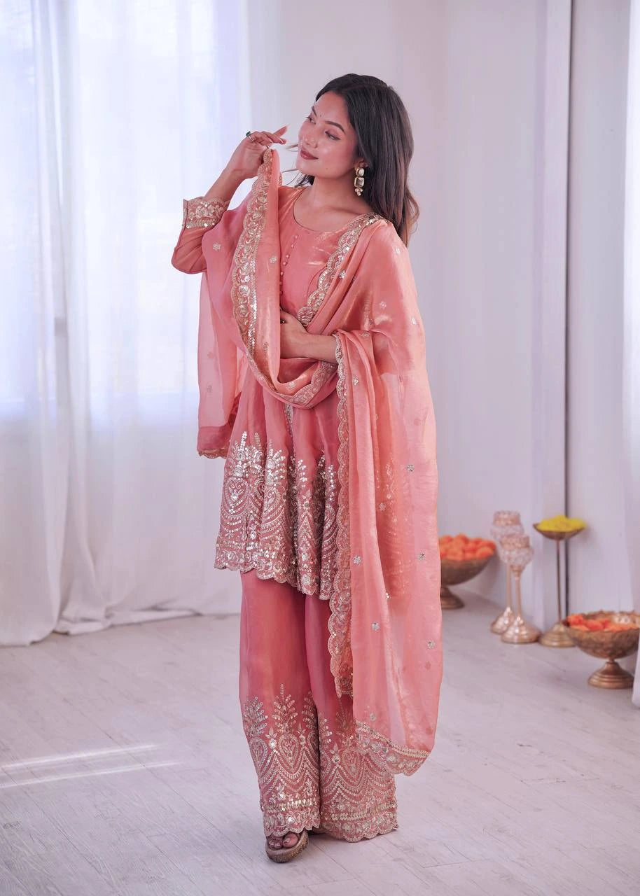 Woman in a traditional pink outfit with gold embroidery in a minimalistic setting.
