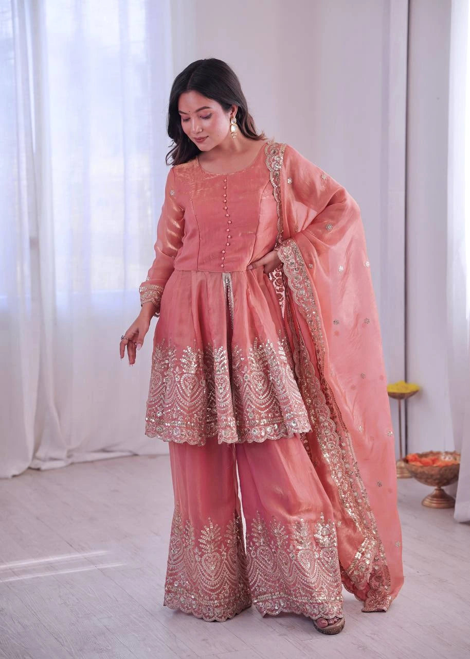 Woman in a traditional pink outfit with gold embroidery standing indoors.