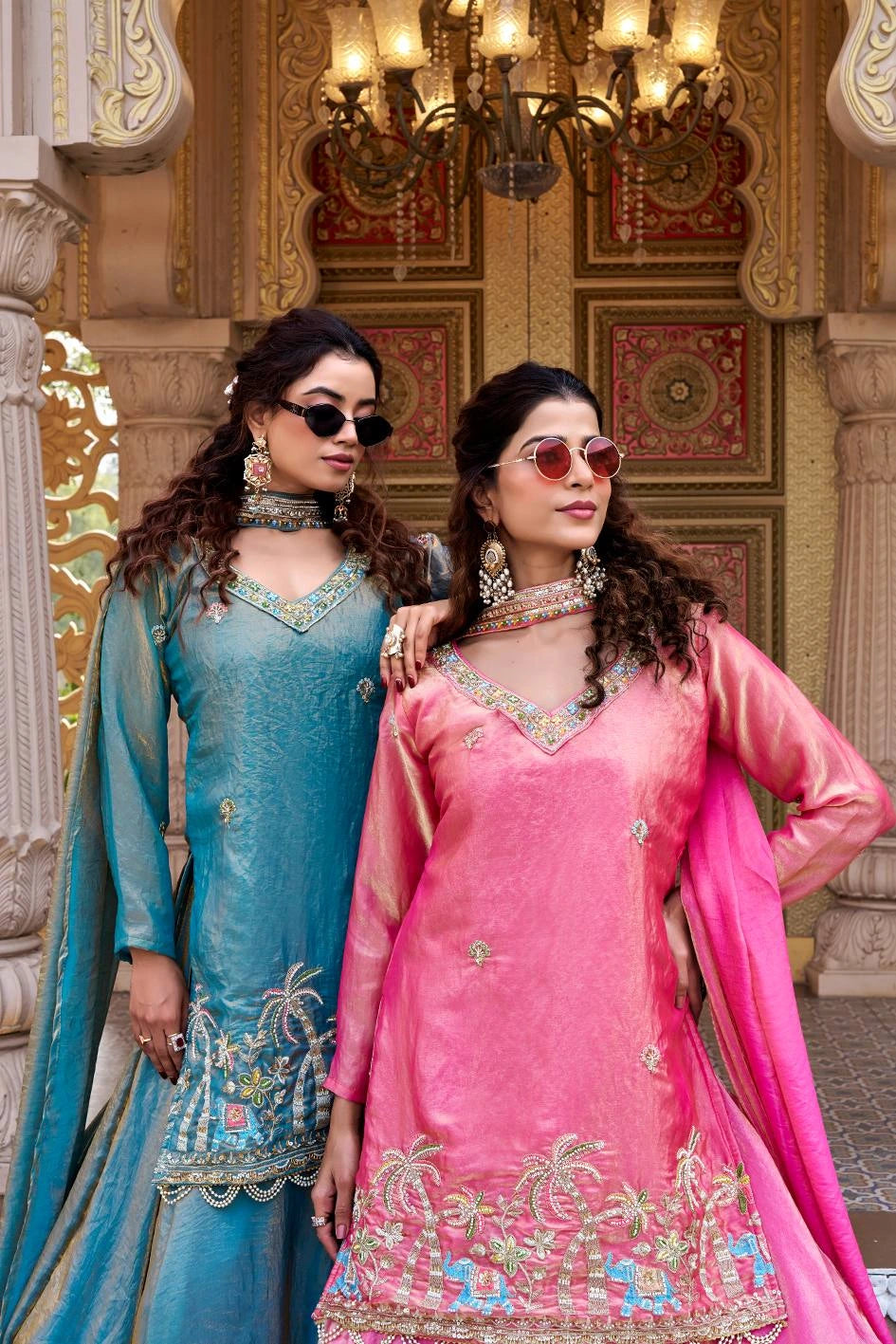 A woman stands gracefully on palace-style steps wearing a bright pink traditional outfit.
