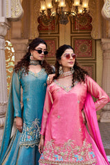 A woman stands gracefully on palace-style steps wearing a bright pink traditional outfit.
