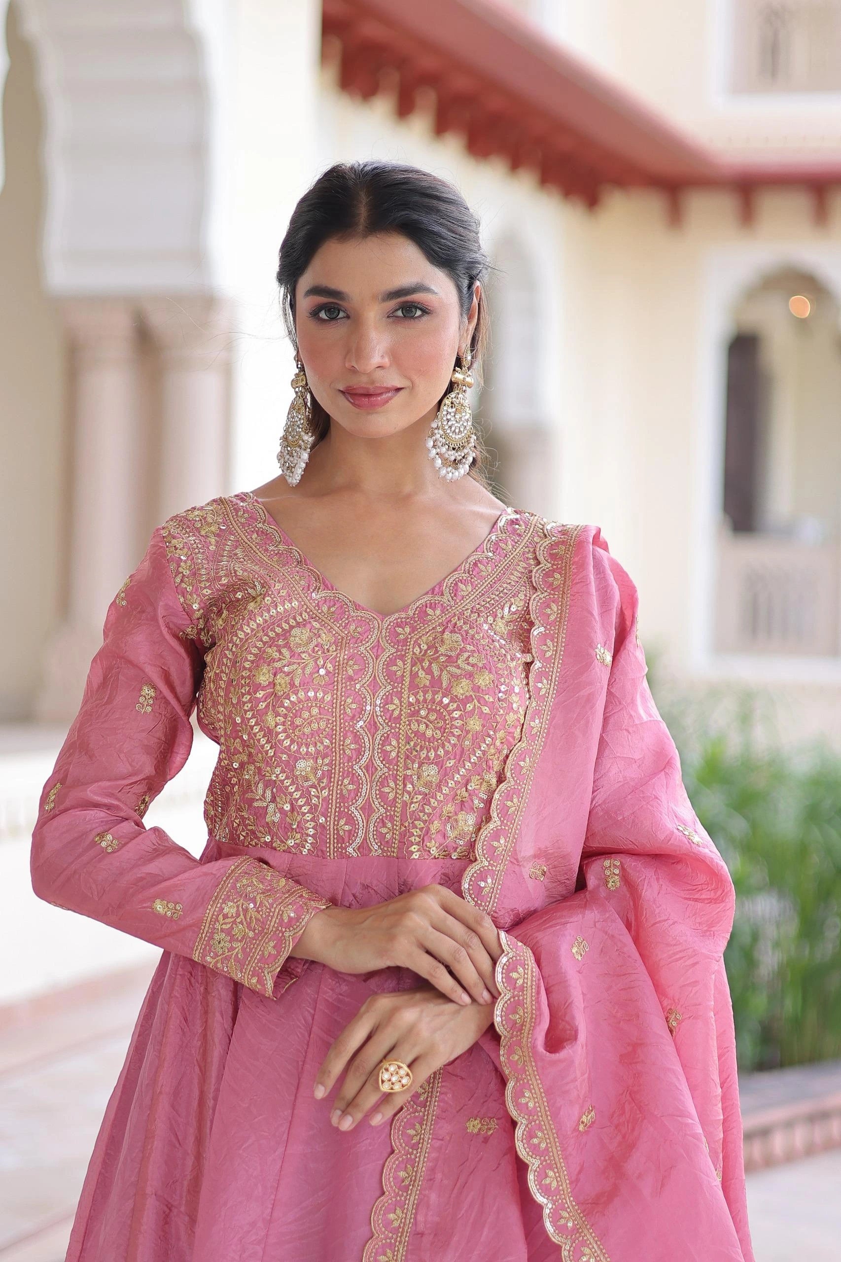 Woman wearing a pink traditional outfit with gold embroidery in an outdoor setting.